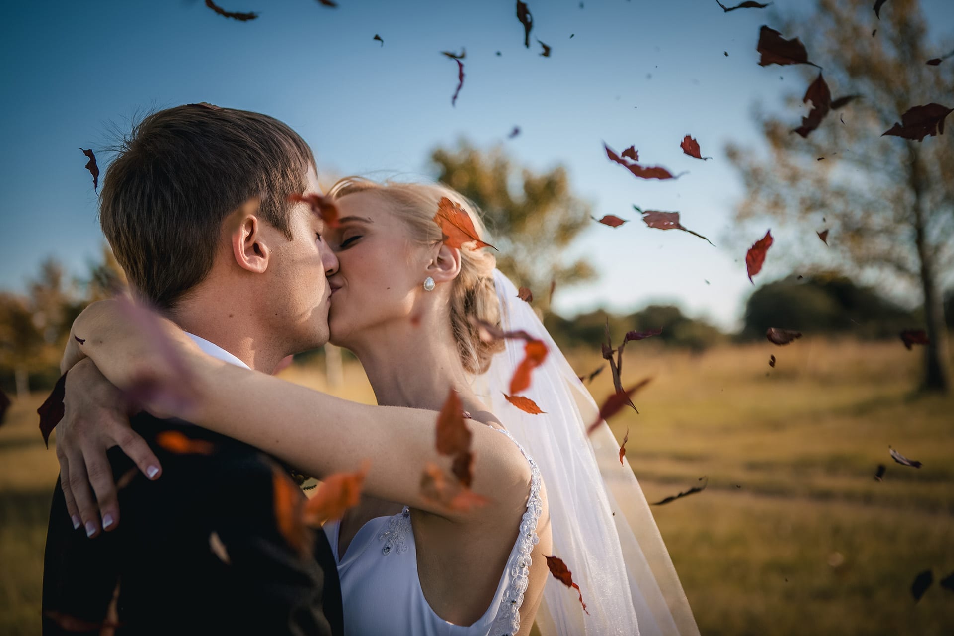A newly married couple kissing as autumn leaves move around them