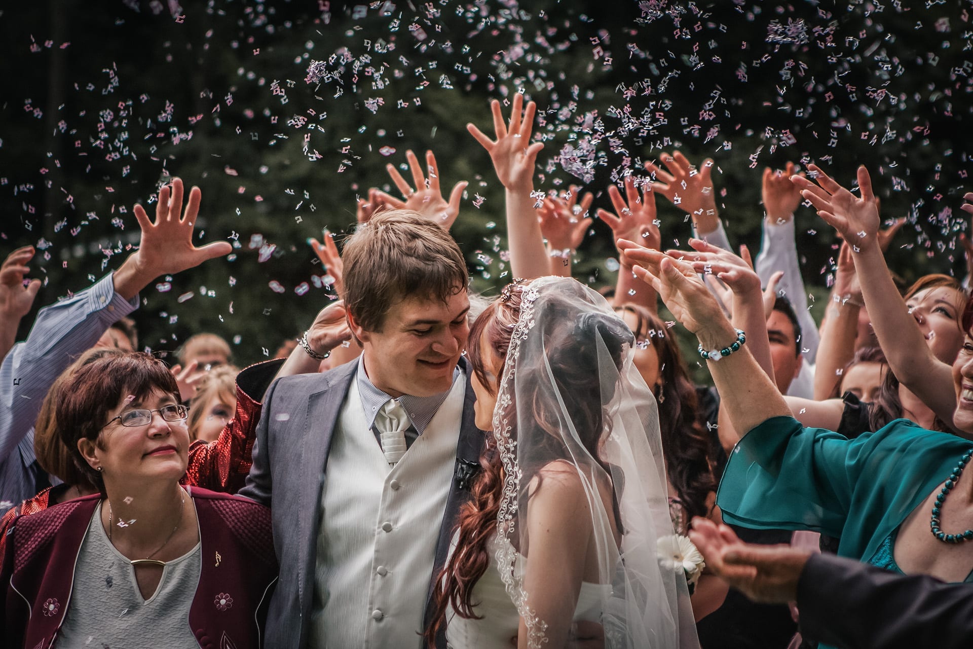 A newly married couple smiling at each other while guests throw confetti around them
