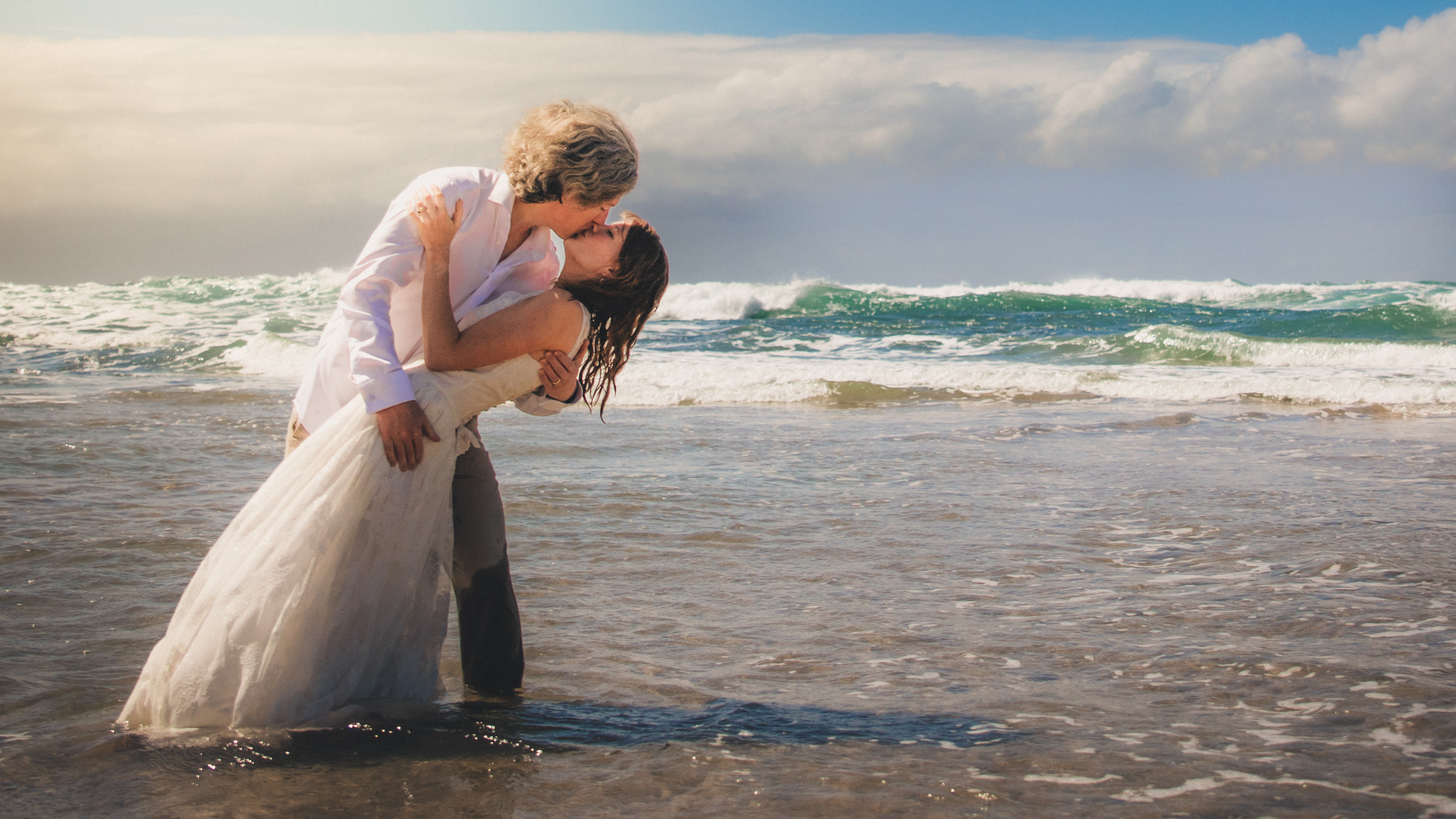 Romantic coastal wedding portrait of a couple kissing in the waves during a destination-style beach shoot