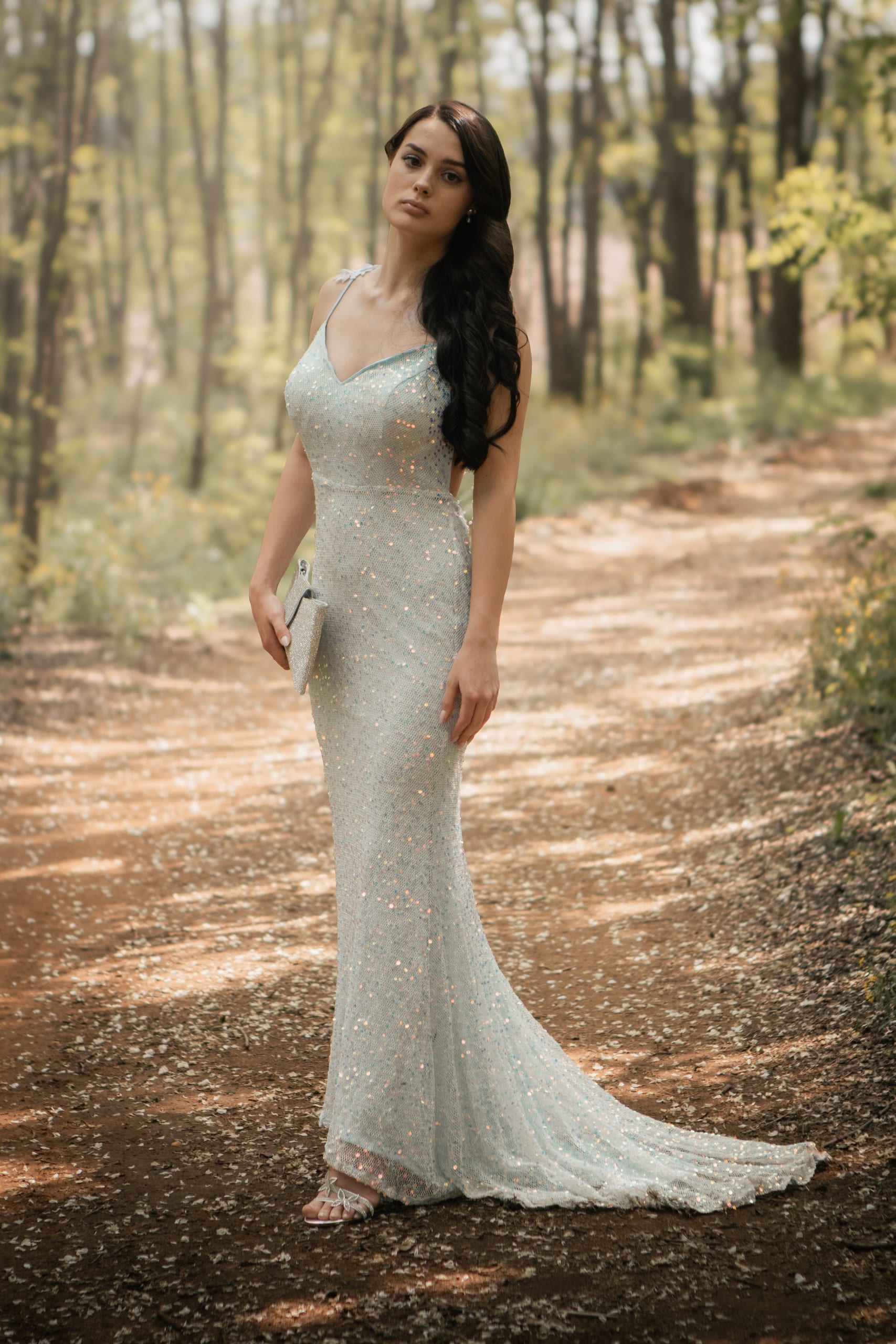 Matriculant posing alone in a silver-blue dress on a wooded path