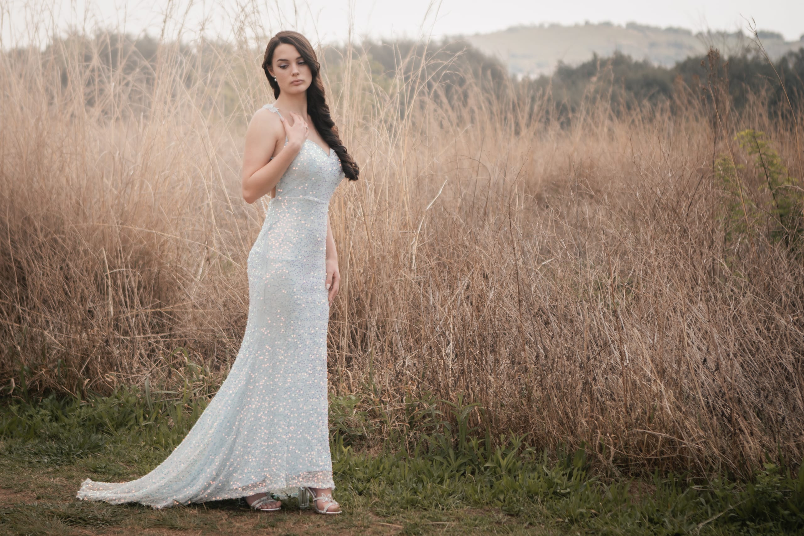 Matriculant standing in a silver-blue dress beside tall dry grass