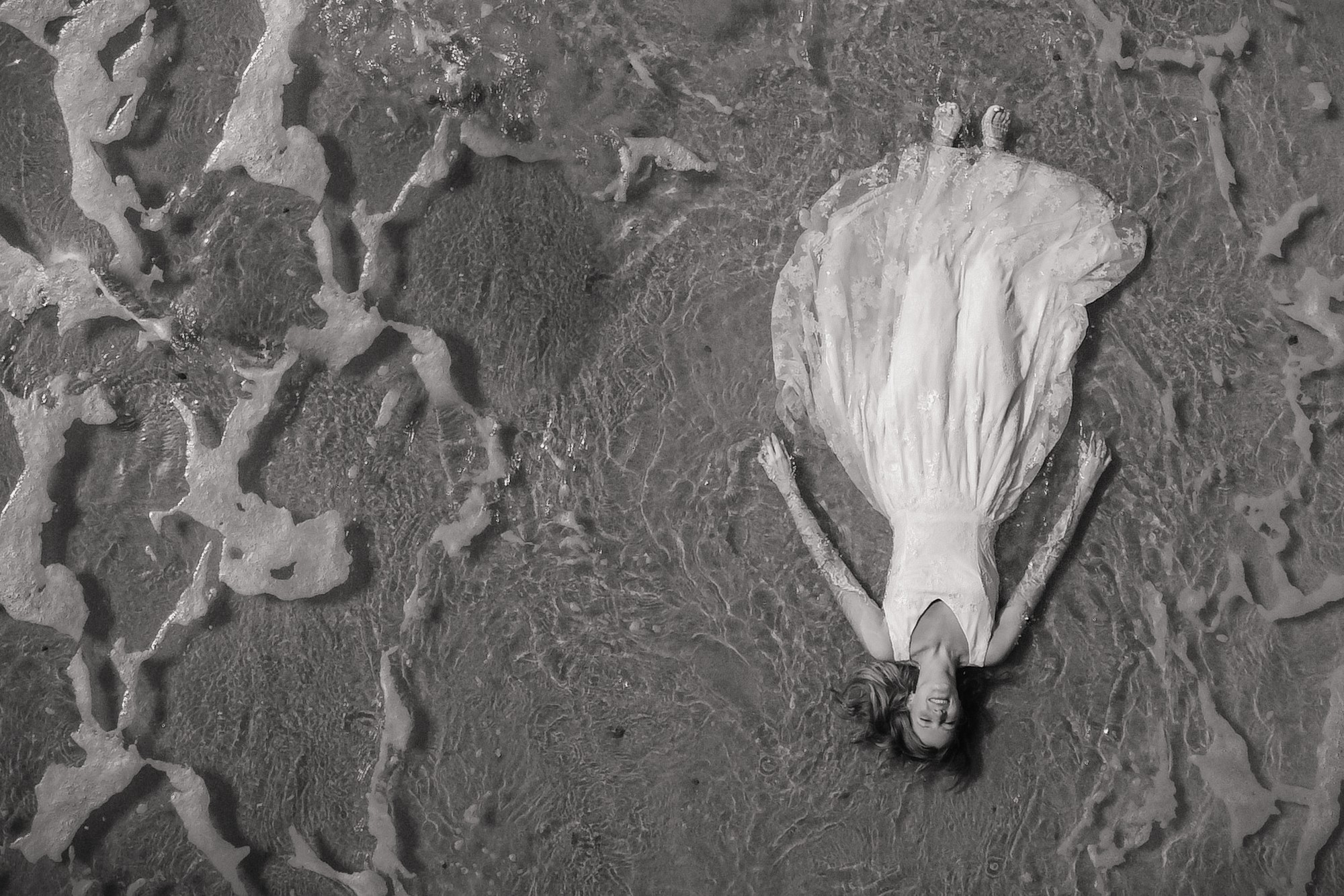 Aerial black and white portrait of a bride lying by the shoreline
