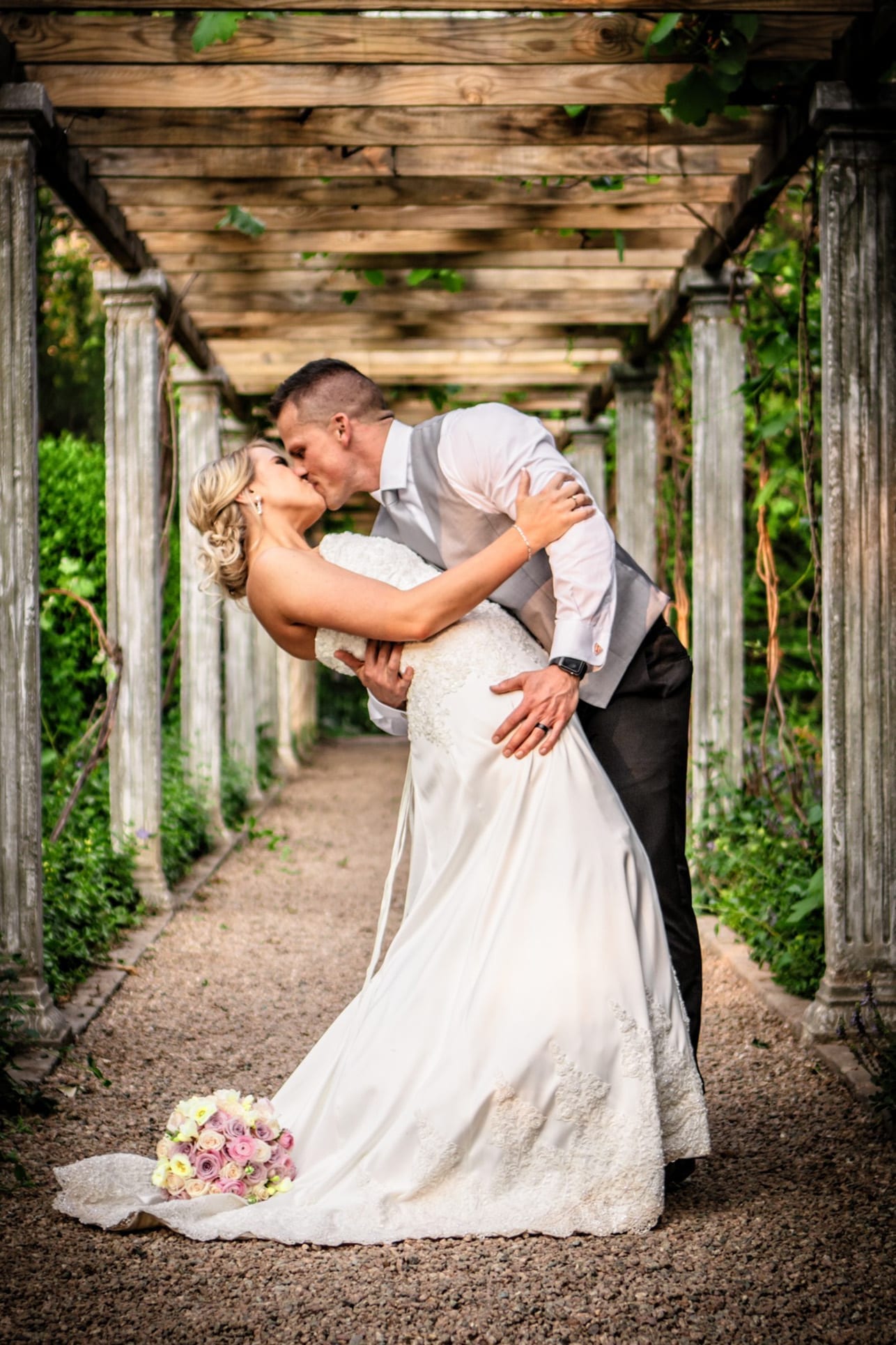 A newly married couple sharing a directed wedding portrait beneath a wooden pergola