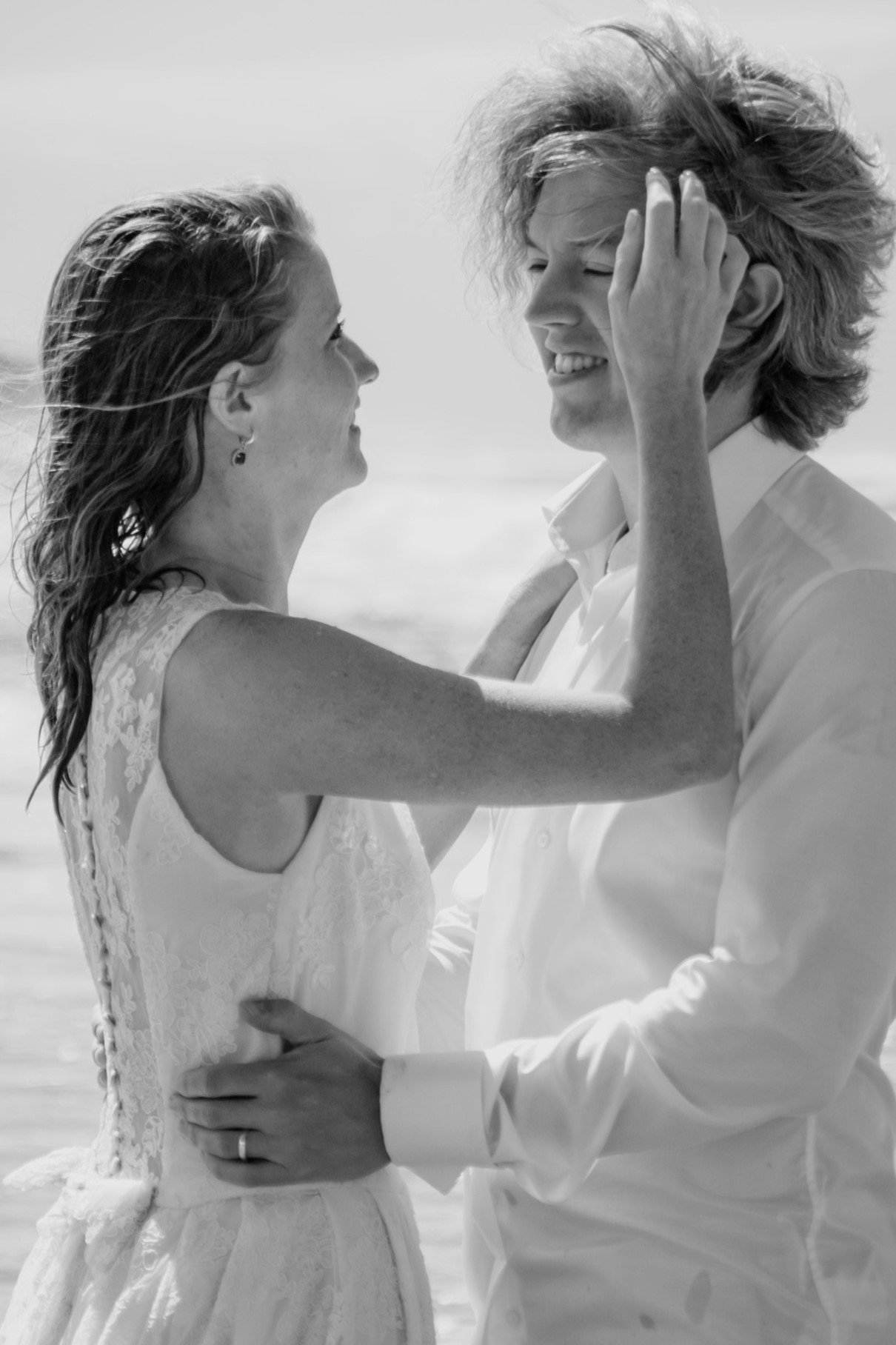Bride and groom laughing together on a windy beach during a candid wedding portrait