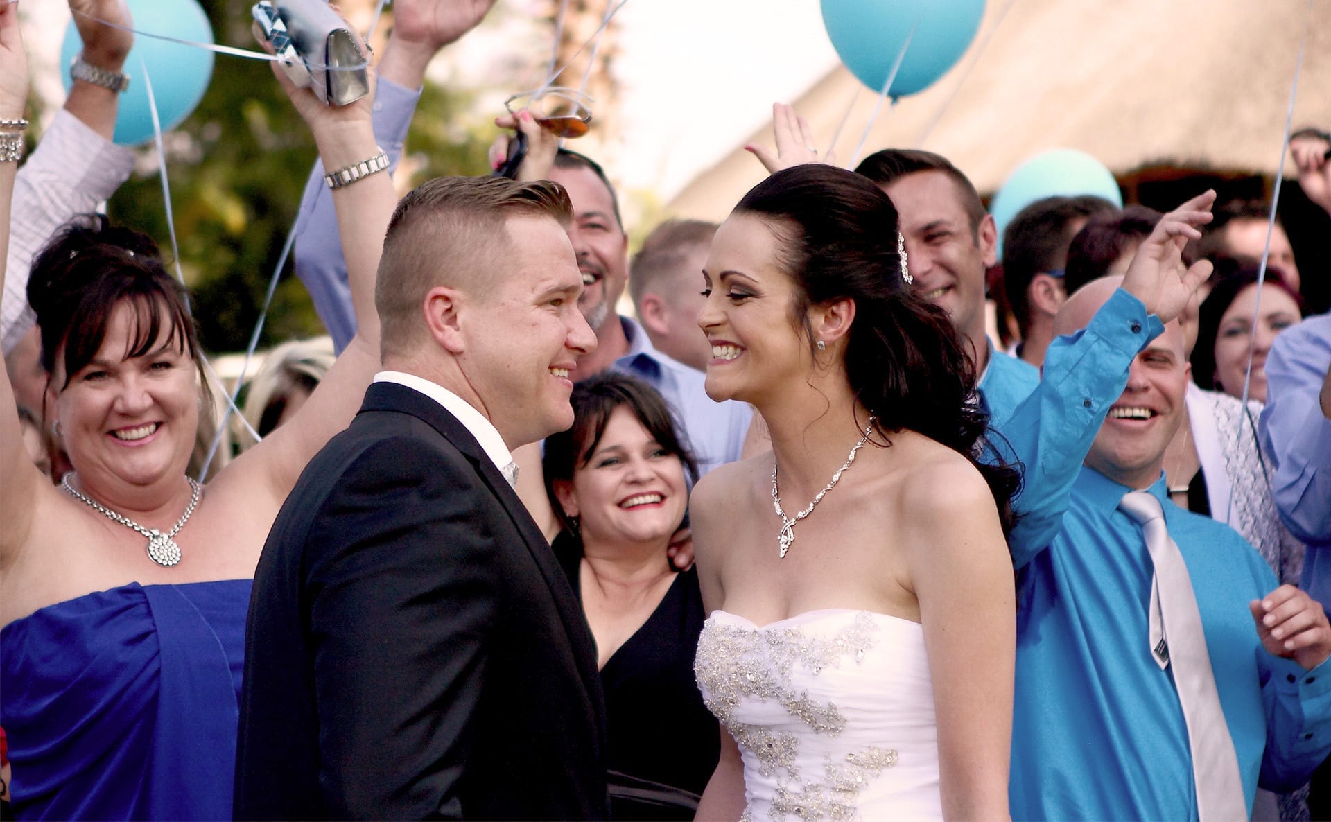 A newly married couple smiling at each other while their wedding guests celebrate around them
